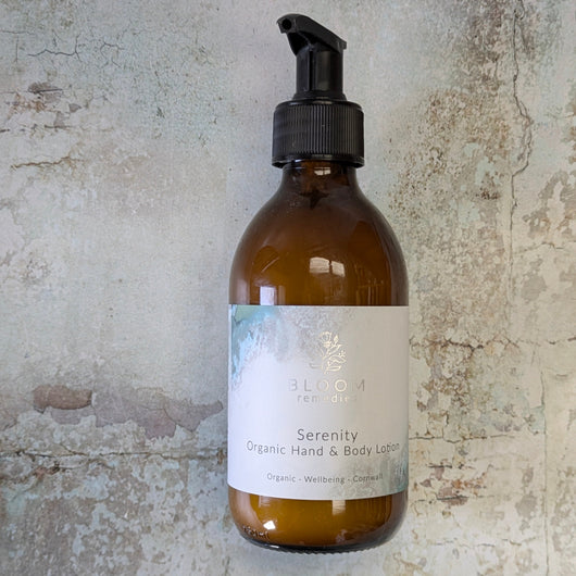 Amber glass bottle with pump dispenser labeled 'Serenity Organic Hand & Body Lotion' on a textured stone background.