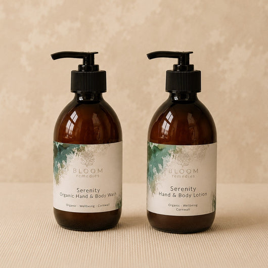 Two amber glass pump bottles of Bloom remediess 'Serenity' Organic Hand & Body Wash and Hand & Body Lotion on a textured beige surface against a matching beige background.