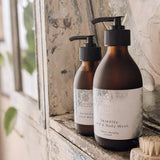 Two bottles of 'Serenity' hand and body wash by Bloom Remedies on a window sill.